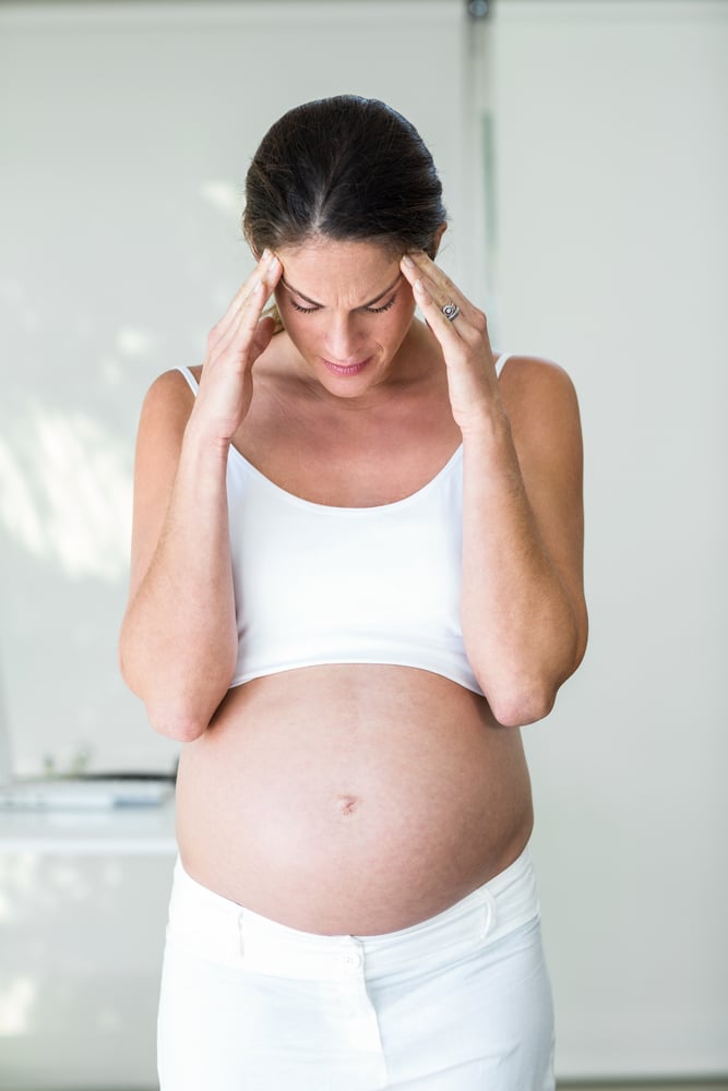 Pregnant woman standing at home with headache